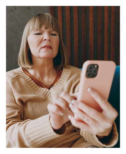 Older woman squinting while looking at her phone.