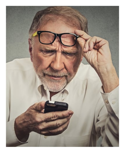 Man holding his eyeglasses while looking at his phone.