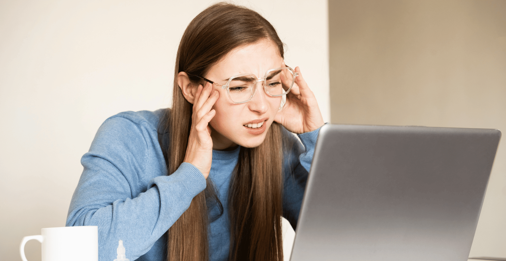 Young woman with dry eye stares uncomfortably at a laptop screen.